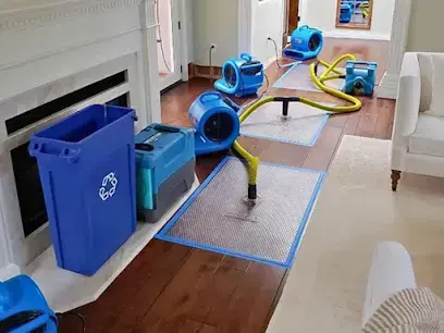 Living room drying with air movers, a drying mat and hoses on a hardwood floor