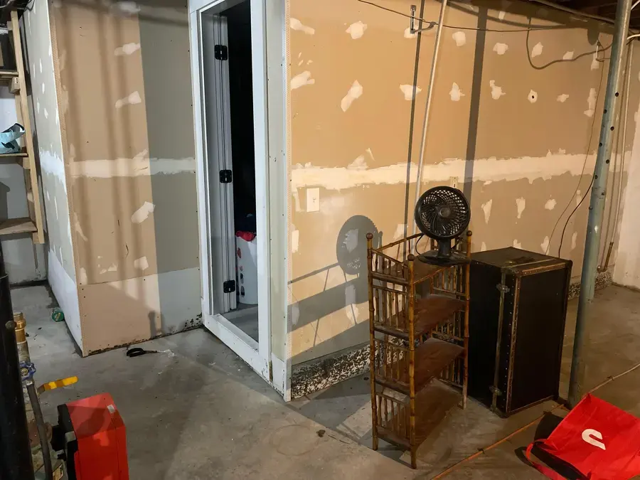 Basement room with the walls opened, a fan running and stored furniture moved aside