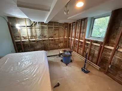 Room with the walls opened to the studs, plastic sheeting and a wet vacuum during drying