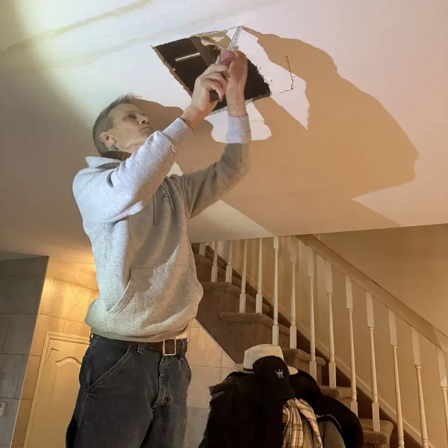 Technician opening a water-damaged ceiling above a staircase in a Union, NJ home